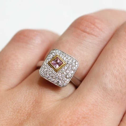 Plat and 18k yellow ring with bezel set 0.25ct pink princess cut sapphire surrounded by pave set diamonds.