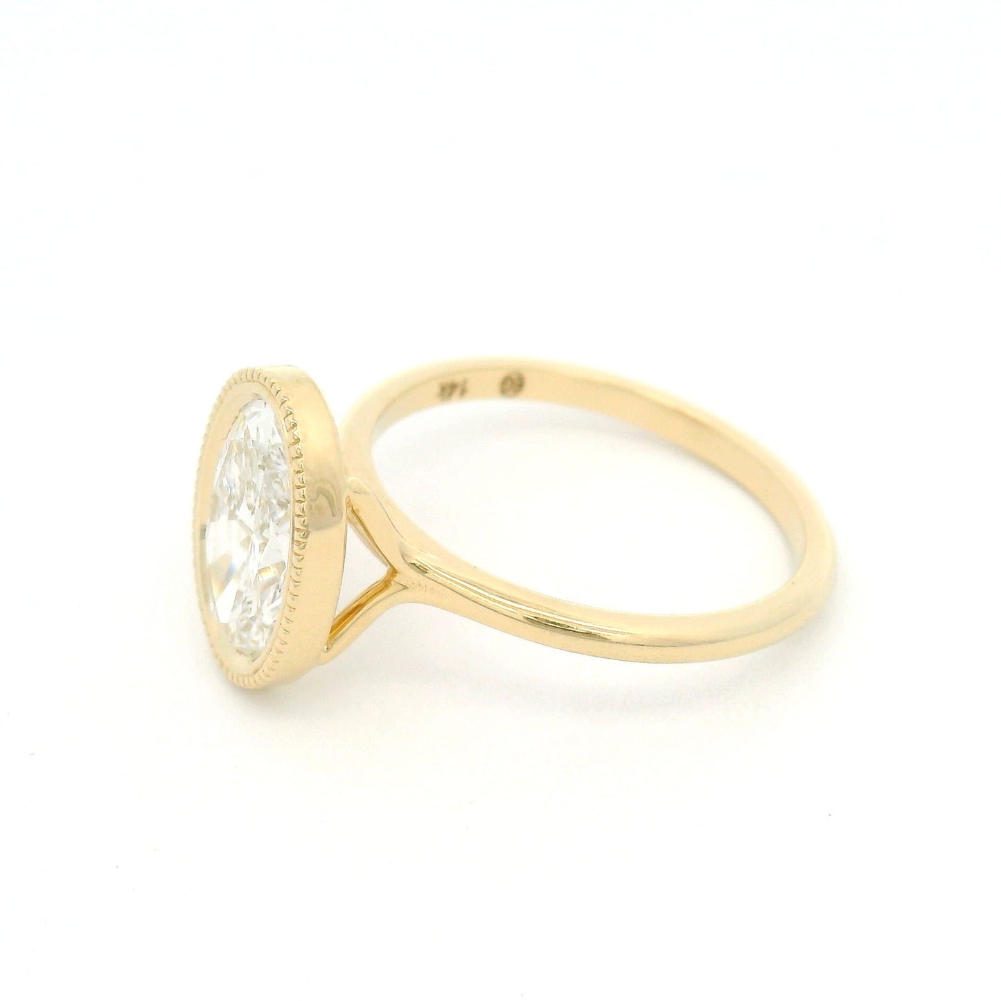 14K yellow gold bezel-set solitaire engagement ring with lab-grown 2ct oval brilliant-cut diamond, milgrain detailing, and softly domed 1.8mm band.