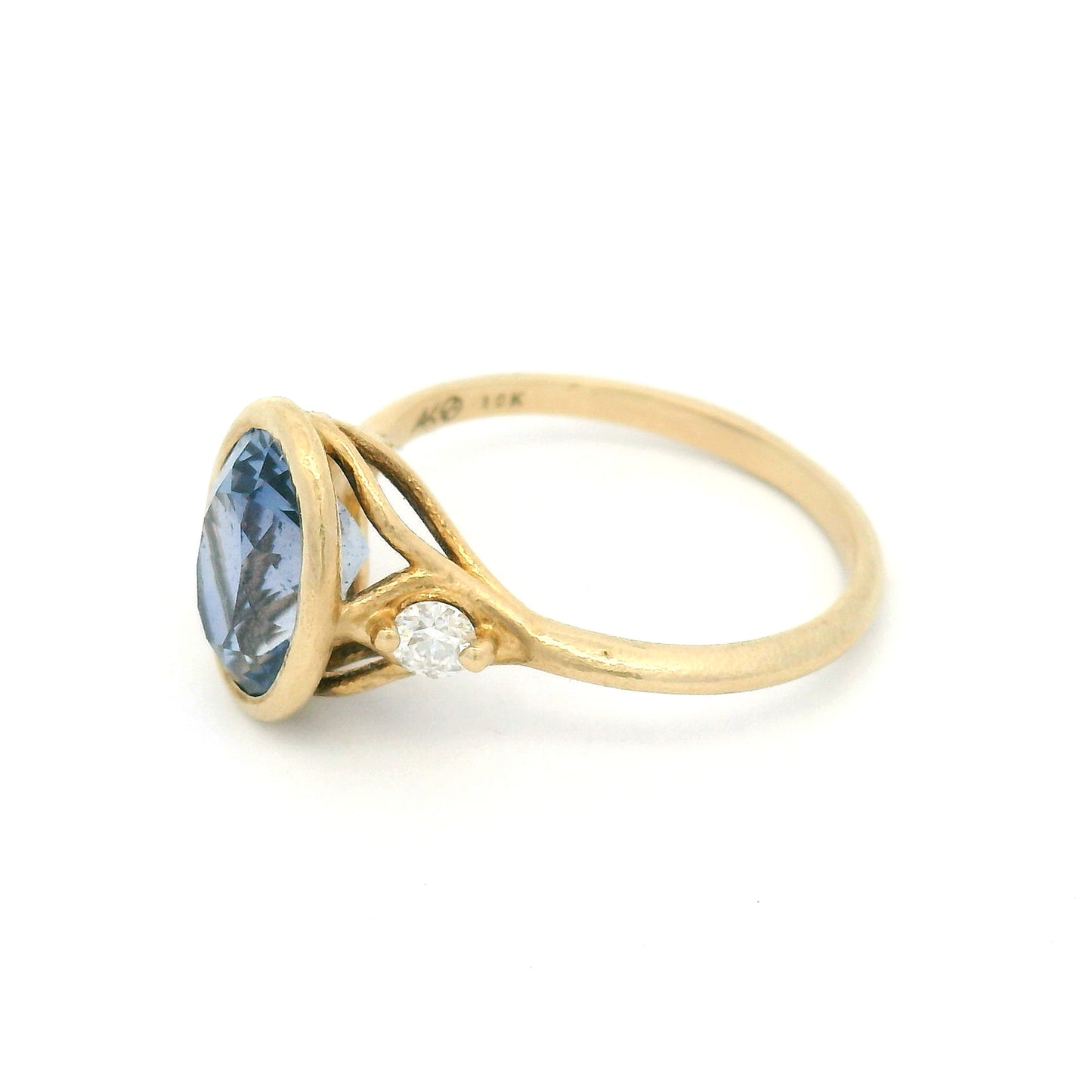 10K yellow gold organic three-stone engagement ring with a bezel-set 3ct lab-grown oval blue sapphire and two claw-set moissanite shoulder stones.