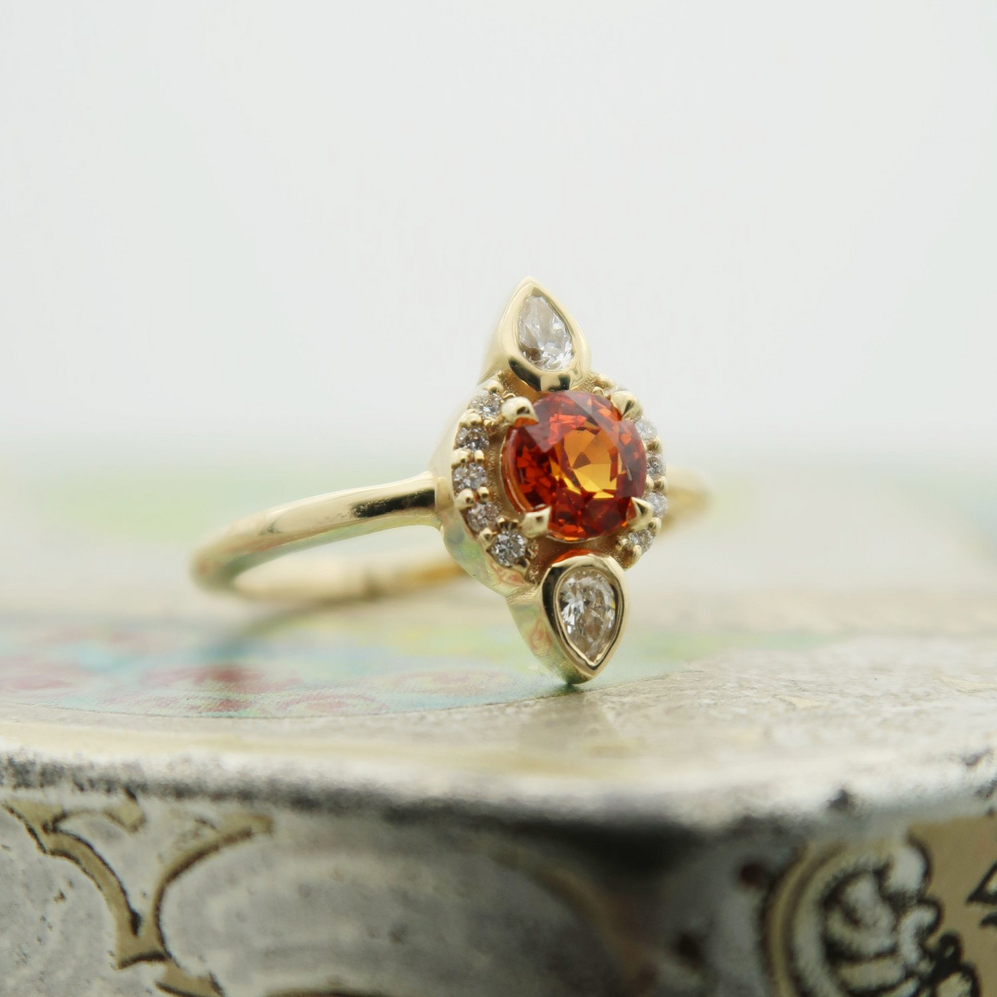 14K 0.65ct orange sapphire lab diamond accent engagement ring. Resting on a tile.