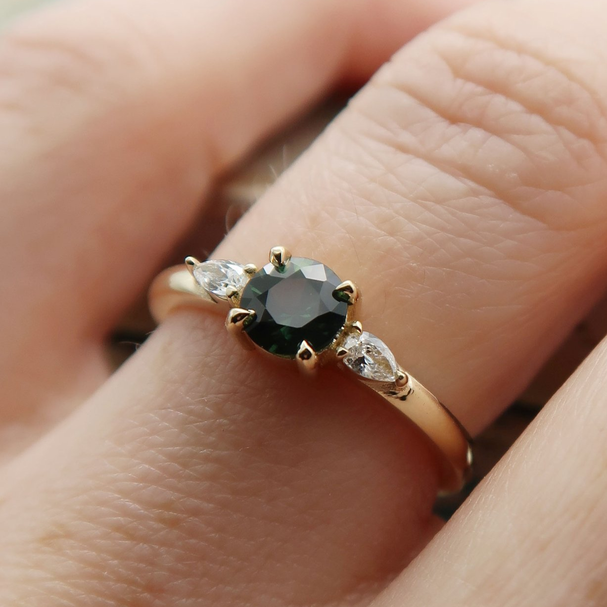 14k Yellow Teal-Green Sapphire Ring with Pear Lab Diamonds On The Side. Worn on a hand.