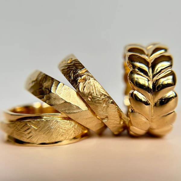 Hand Carved Band, 6mm wide, half round crafted in 14K Yellow. Displayed with 3 other gold bands.