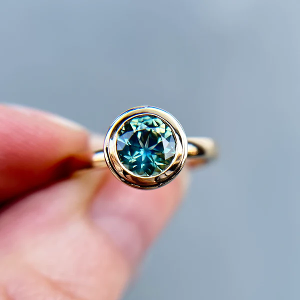 14k Yellow gold round teal sapphire Canadian engagement ring held in fingers