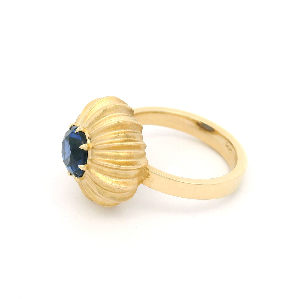 14K yellow gold claw-set solitaire engagement ring featuring a 6.6mm lab-grown round blue sapphire in a sculptural fluted sunburst setting.