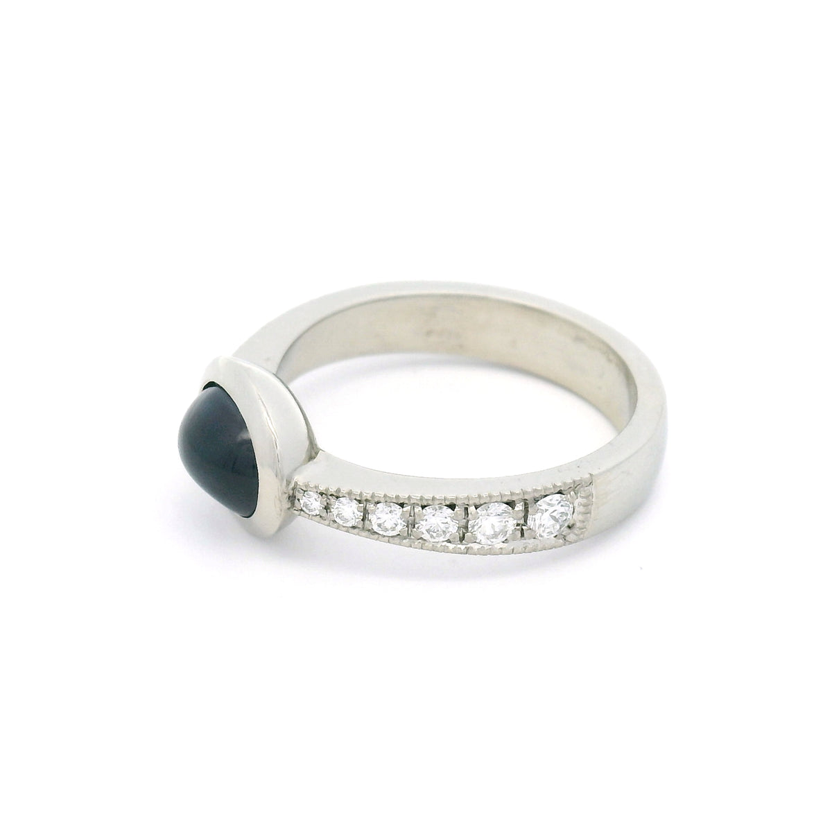 18K white gold bezel-set engagement ring with a natural 2.23ct oval cabochon blue sapphire and tapered band featuring 12 natural round brilliant-cut diamonds.