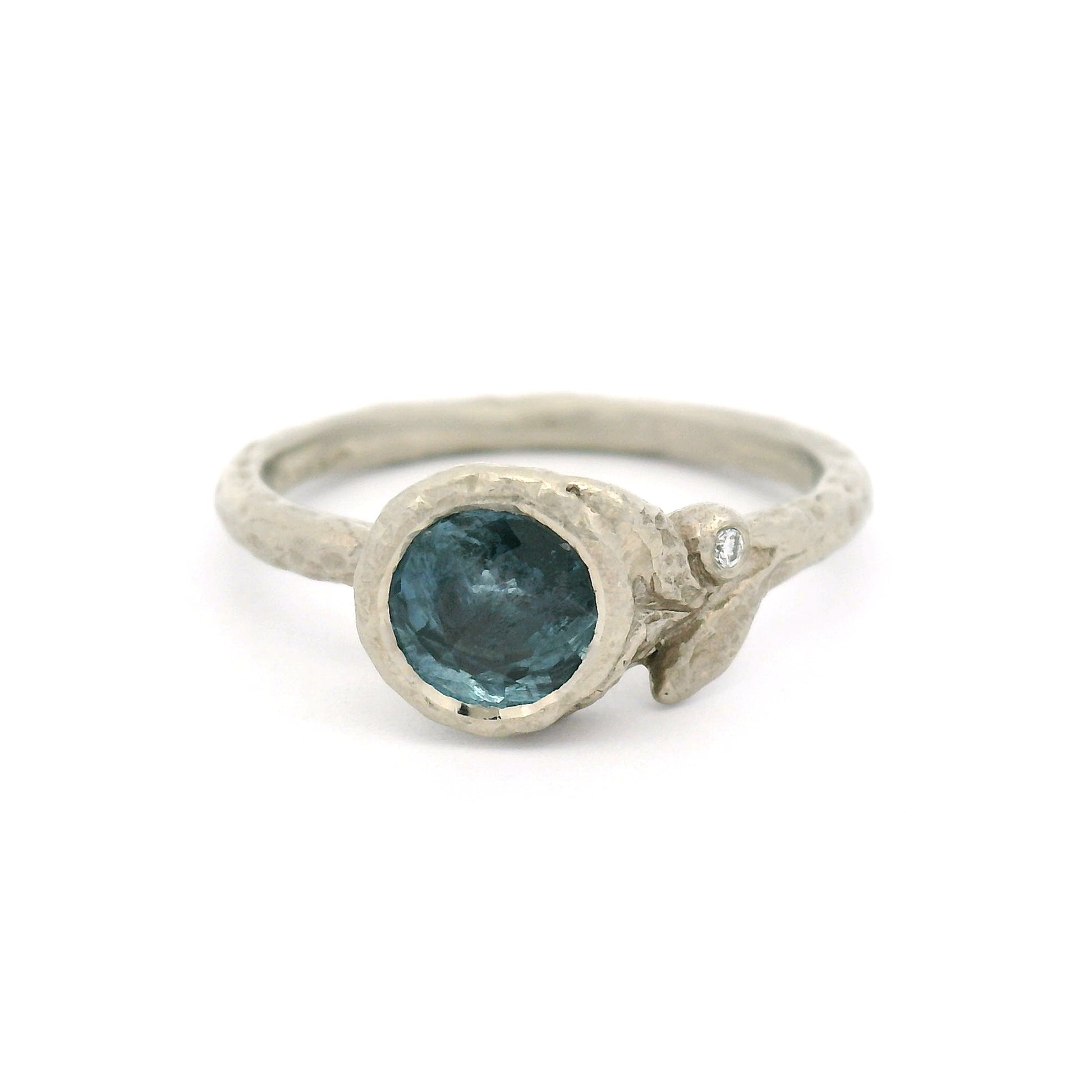 10K white gold organic textured engagement ring with bezel-set 0.93ct round bluish-grey sapphire, asymmetrical carved leaves, and bezel-set diamond accent.
