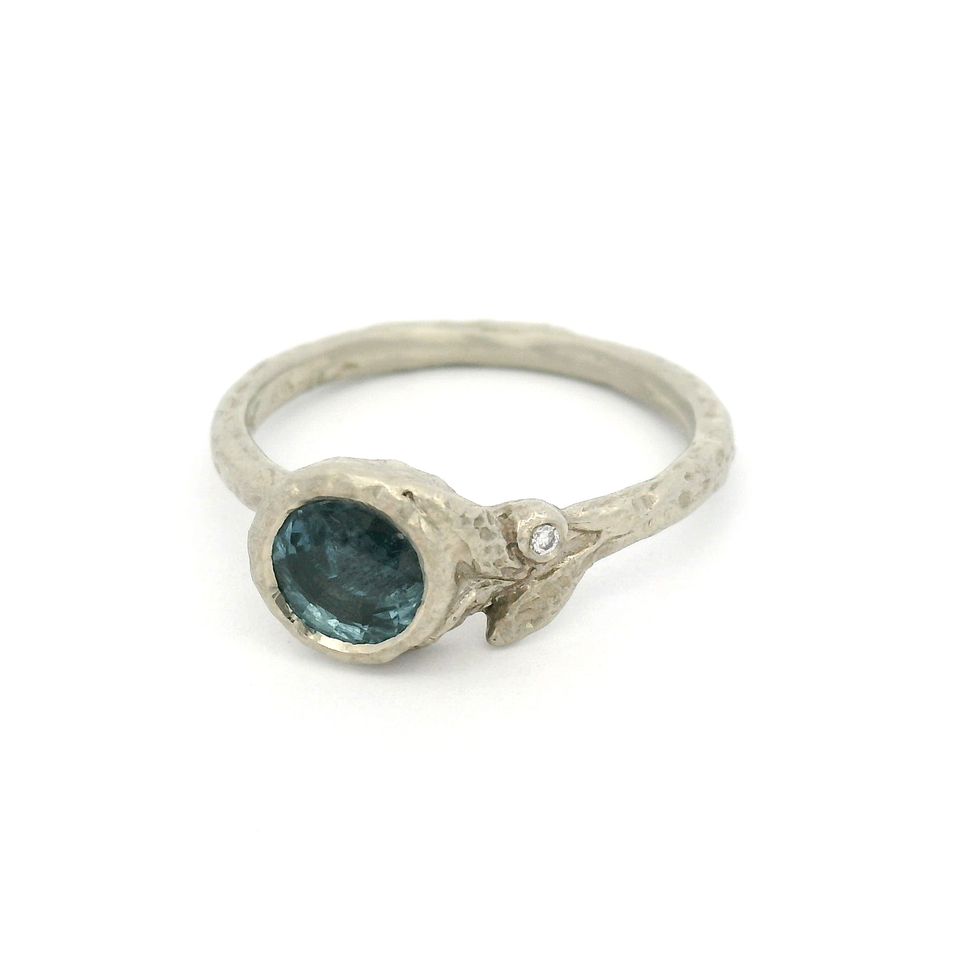 10K white gold organic textured engagement ring with bezel-set 0.93ct round bluish-grey sapphire, asymmetrical carved leaves, and bezel-set diamond accent.