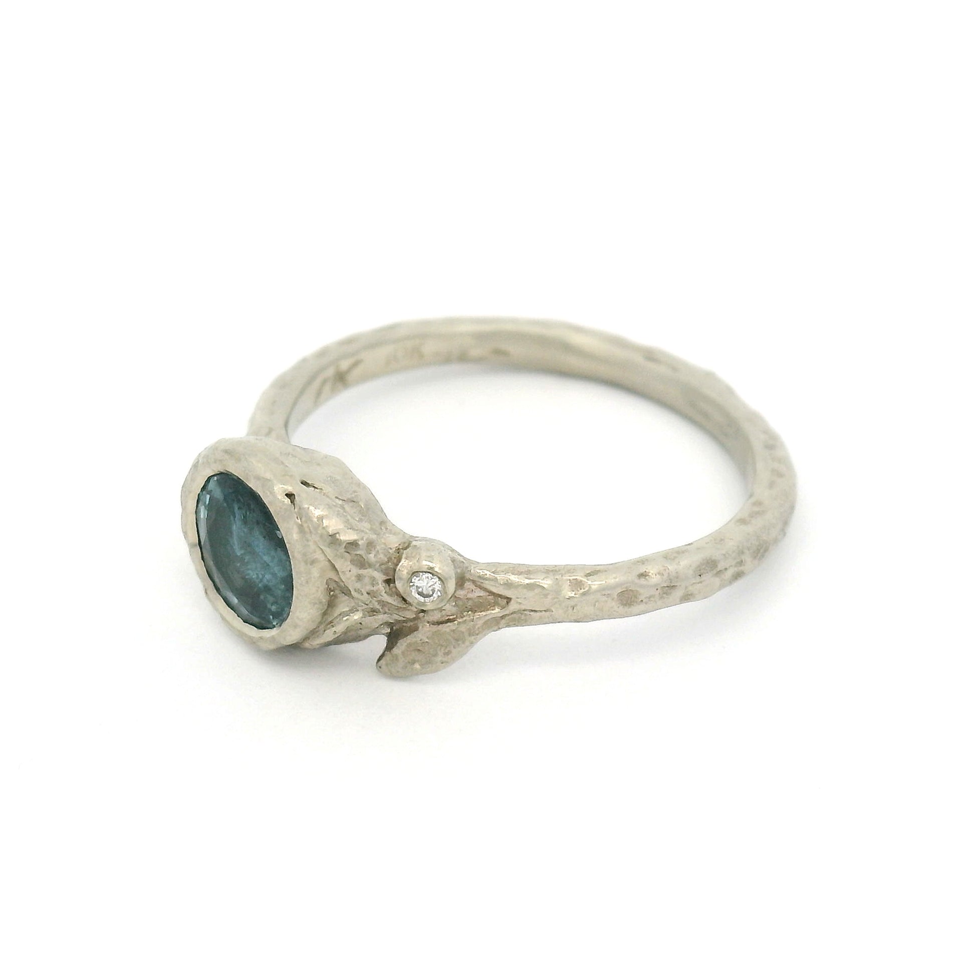 10K white gold organic textured engagement ring with bezel-set 0.93ct round bluish-grey sapphire, asymmetrical carved leaves, and bezel-set diamond accent.