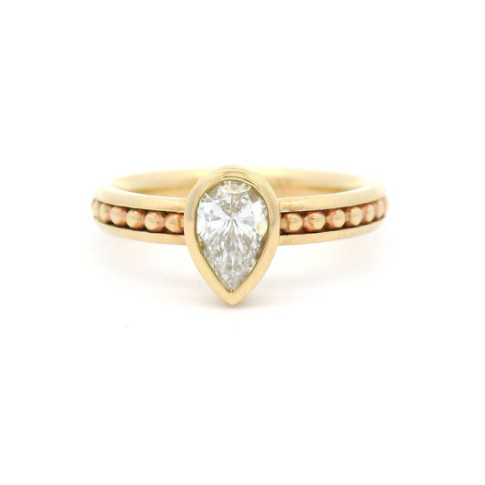 10K yellow gold solitaire engagement ring with a 0.54ct lab-grown pear-shaped diamond, delicate gold bead accents, and channel-set detailing along the band.