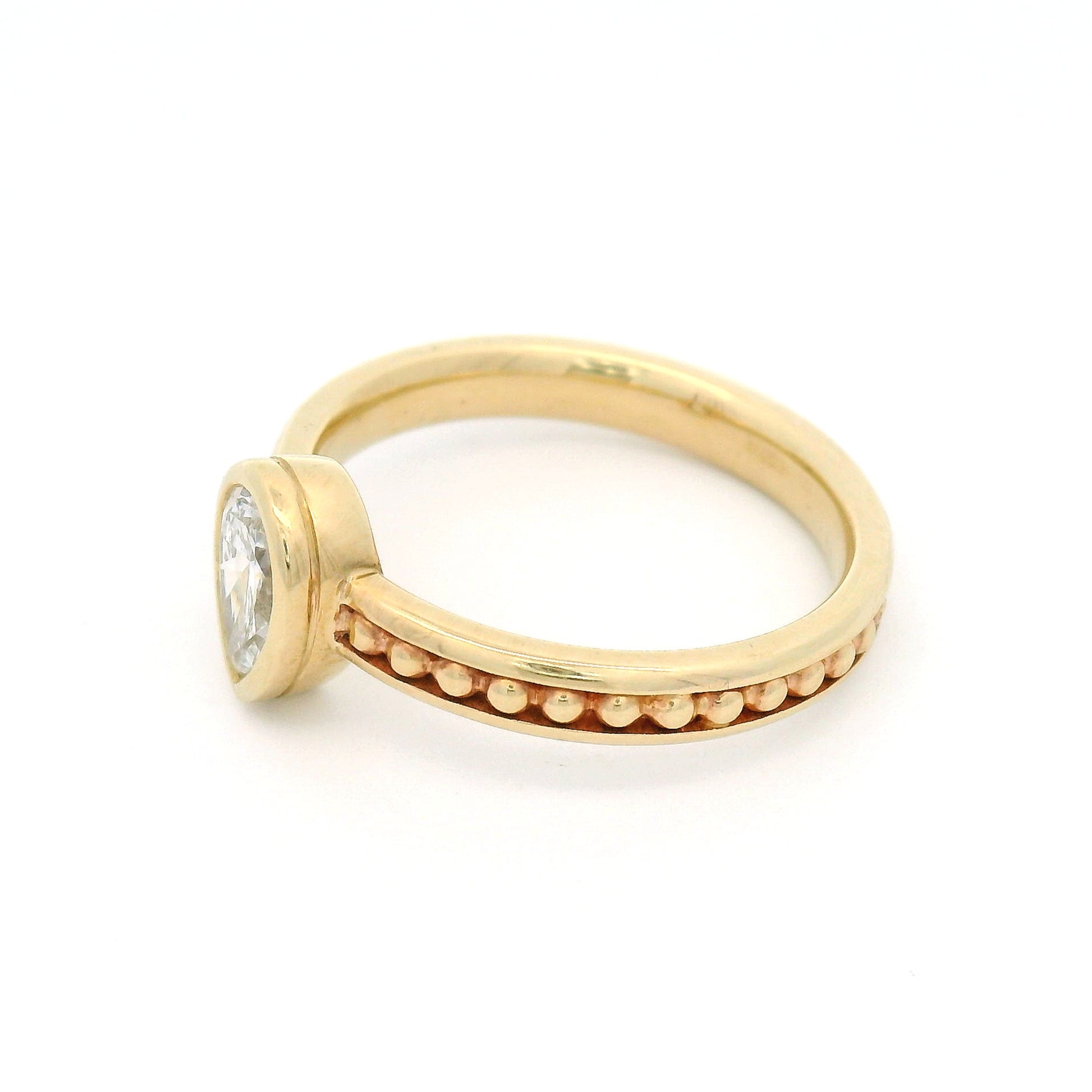 10K yellow gold solitaire engagement ring with a 0.54ct lab-grown pear-shaped diamond, delicate gold bead accents, and channel-set detailing along the band.