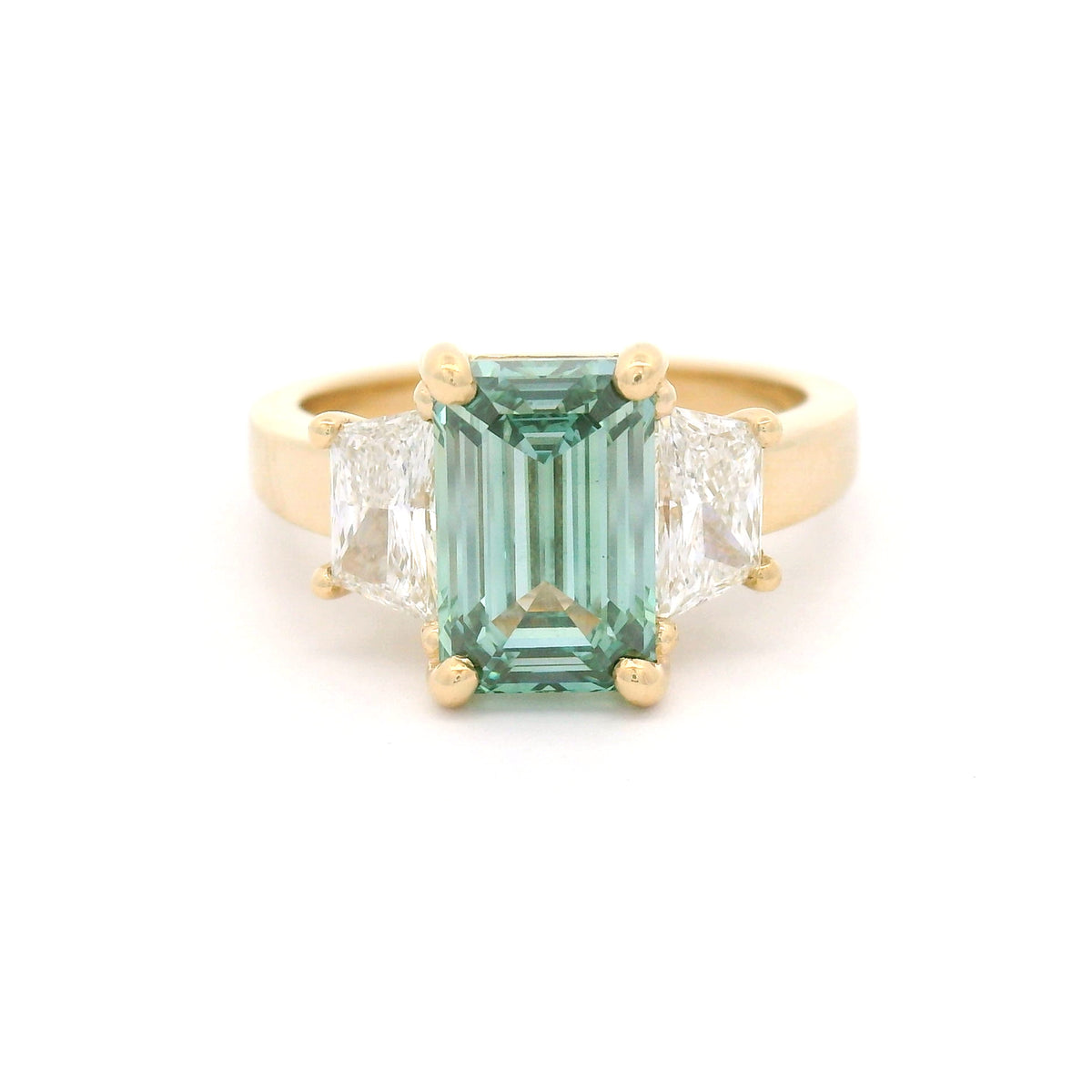 14K yellow gold three-stone engagement ring featuring a claw-set 2.50ct lab-grown green emerald-cut diamond flanked by two lab-grown trapezoid diamonds totalling 0.95cts.