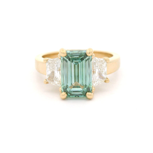14K yellow gold three-stone engagement ring featuring a claw-set 2.50ct lab-grown green emerald-cut diamond flanked by two lab-grown trapezoid diamonds totalling 0.95cts.