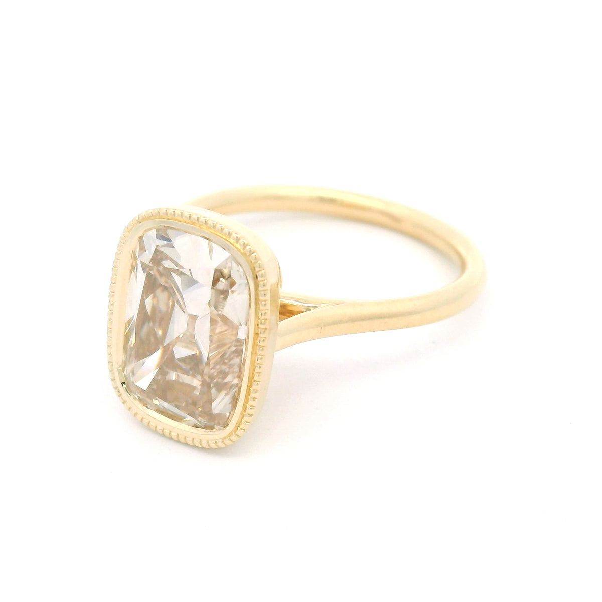 14K yellow gold bezel-set solitaire with a 4.01ct lab-grown cushion old mine-cut diamond in Fancy Light Brown, milgrain bezel and hidden leaf details.