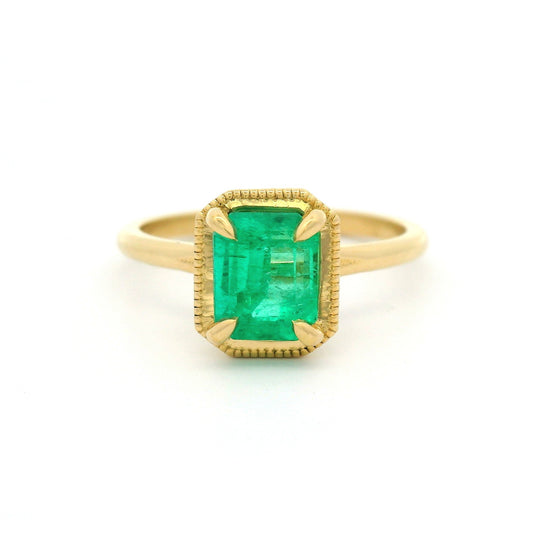18K yellow gold solitaire ring with 1.32ct emerald-cut natural emerald in a 4-claw setting with milgrain-framed detail on a slim band.