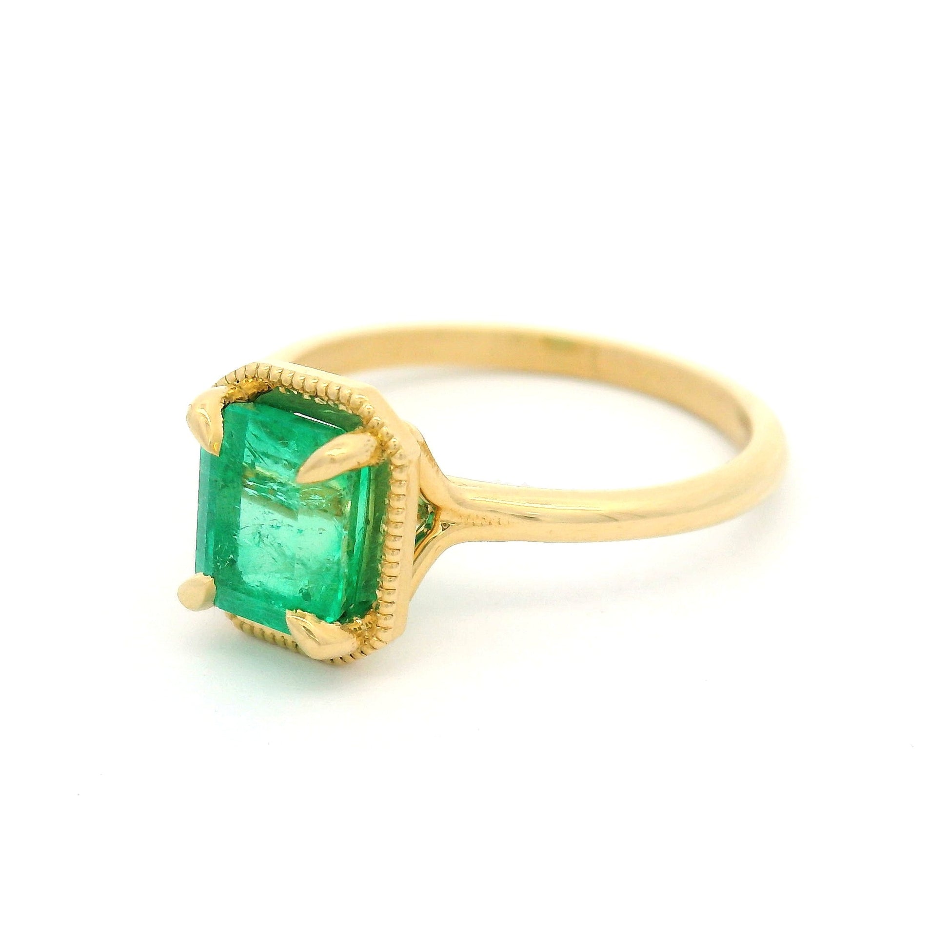 18K yellow gold solitaire ring with 1.32ct emerald-cut natural emerald in a 4-claw setting with milgrain-framed detail on a slim band.