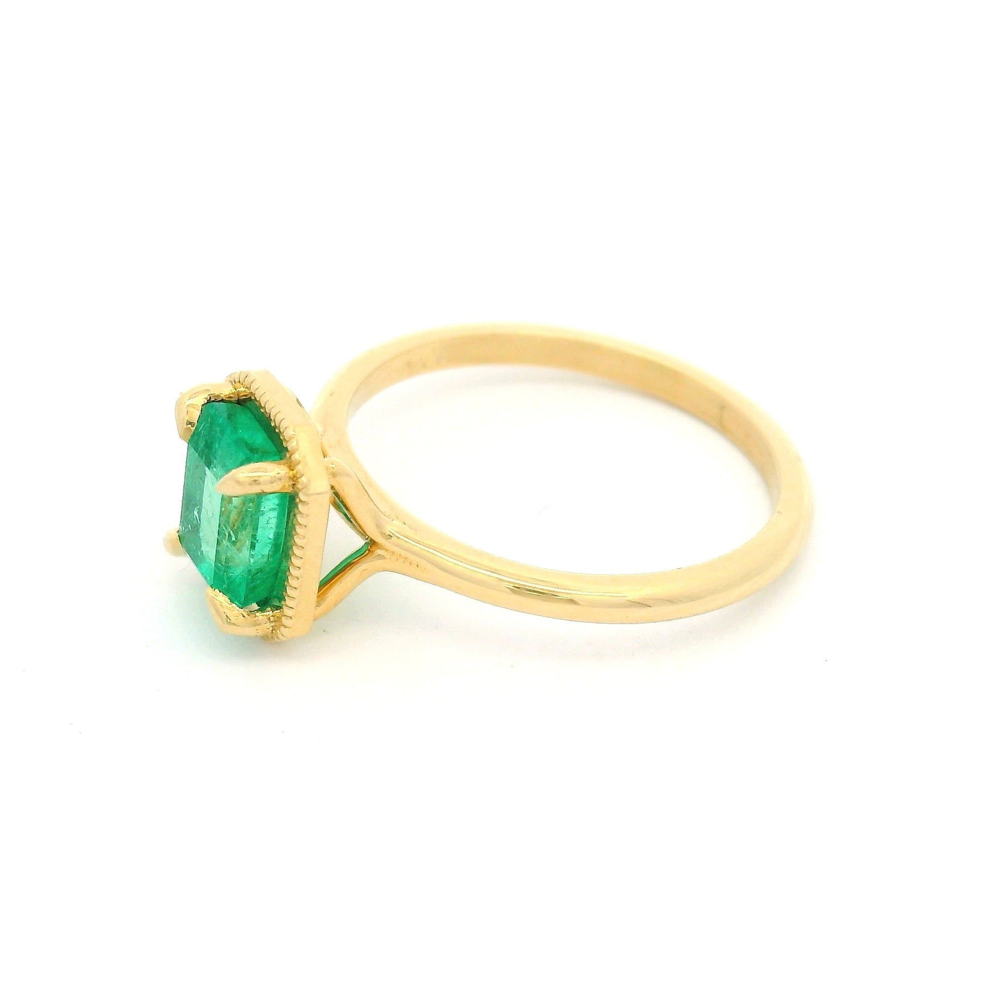 18K yellow gold solitaire ring with 1.32ct emerald-cut natural emerald in a 4-claw setting with milgrain-framed detail on a slim band.