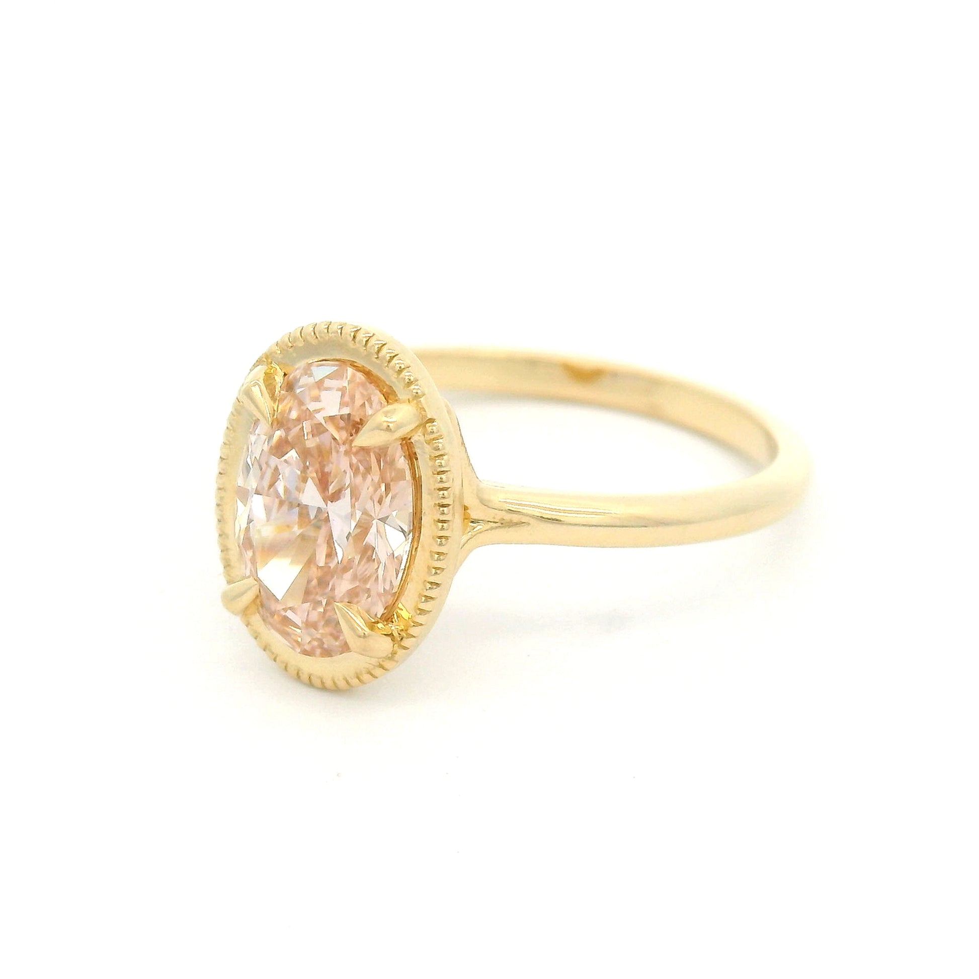 14K yellow gold solitaire engagement ring featuring a 1.50ct lab-grown oval-cut pink diamond in four-claw setting with milgrain edge and 1.8mm band.