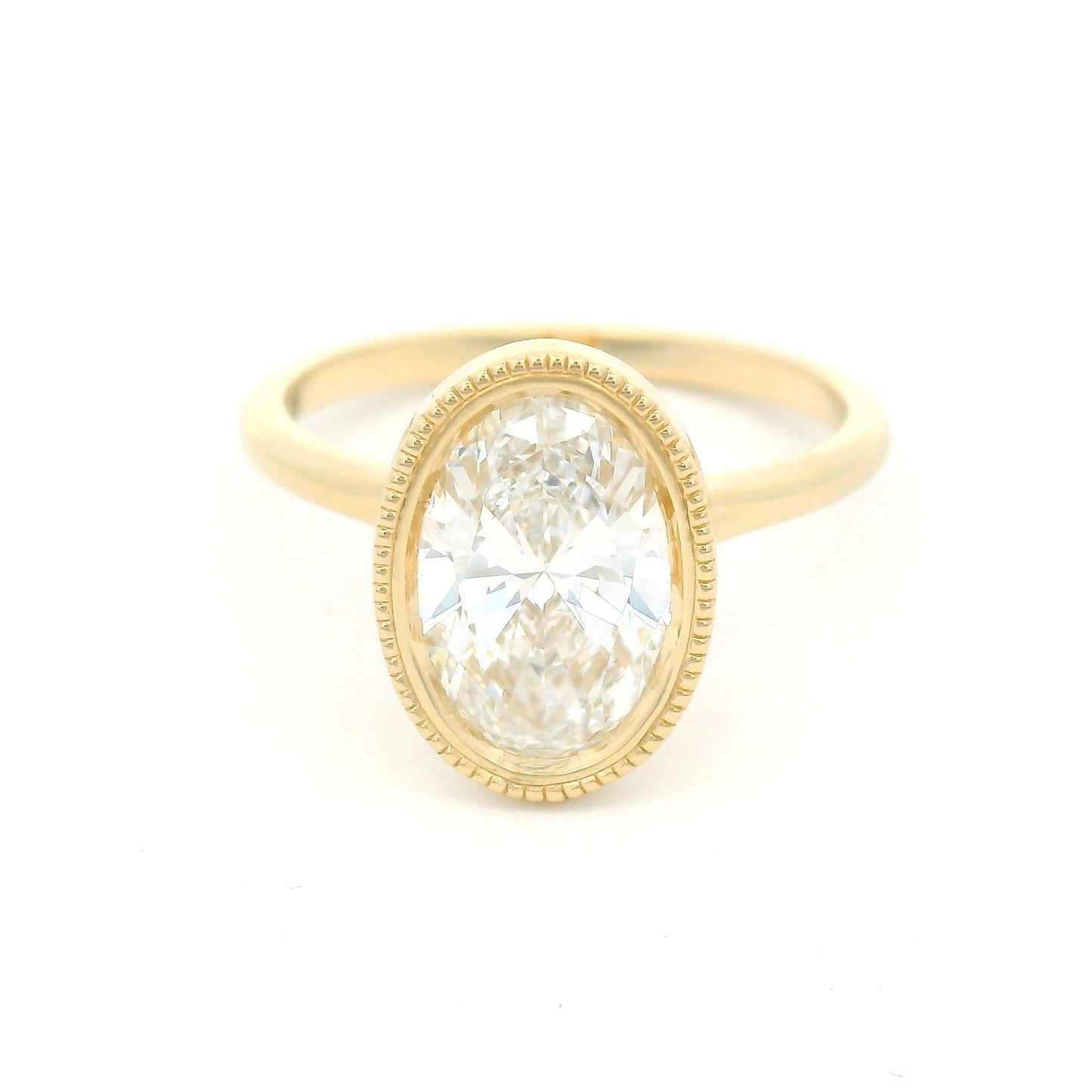 14K yellow gold bezel-set solitaire engagement ring with lab-grown 2ct oval brilliant-cut diamond, milgrain detailing, and softly domed 1.8mm band.