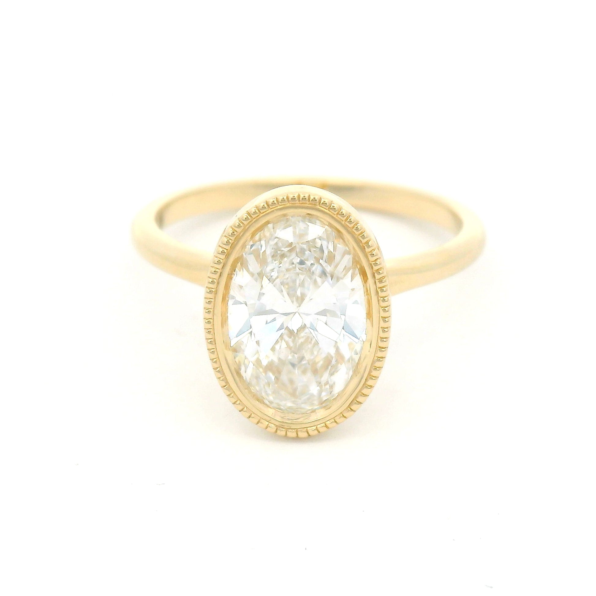 14K yellow gold bezel-set solitaire engagement ring with lab-grown 2ct oval brilliant-cut diamond, milgrain detailing, and softly domed 1.8mm band.
