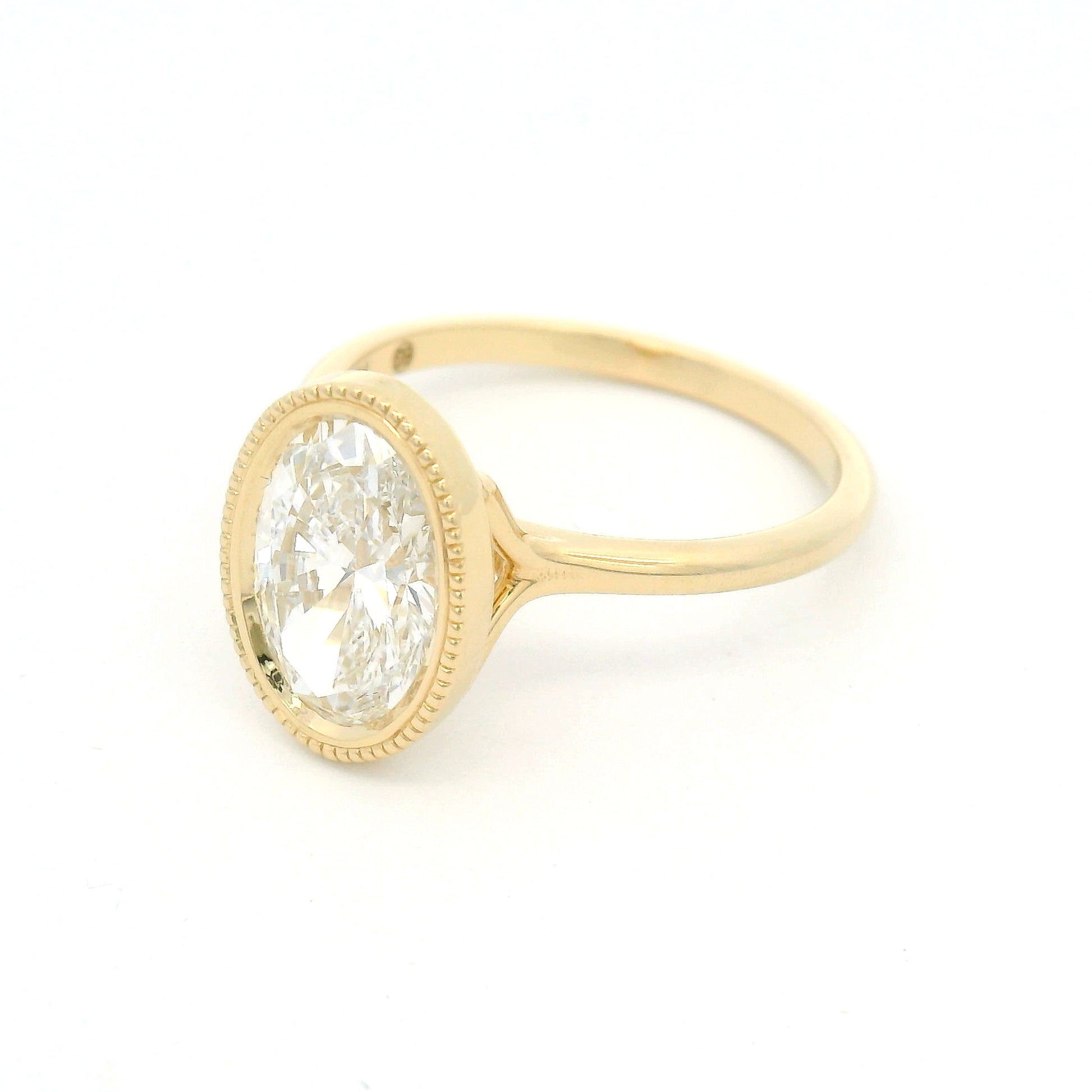 14K yellow gold bezel-set solitaire engagement ring with lab-grown 2ct oval brilliant-cut diamond, milgrain detailing, and softly domed 1.8mm band.