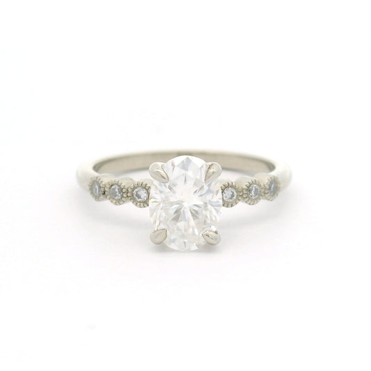 10K white gold engagement ring with a 1.50ct oval moissanite, six bezel-set round brilliant-cut moissanites and fine milgrain details.