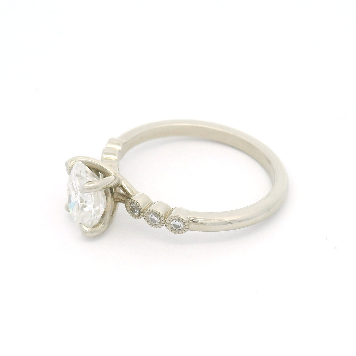 10K white gold engagement ring with a 1.50ct oval moissanite, six bezel-set round brilliant-cut moissanites and fine milgrain details.