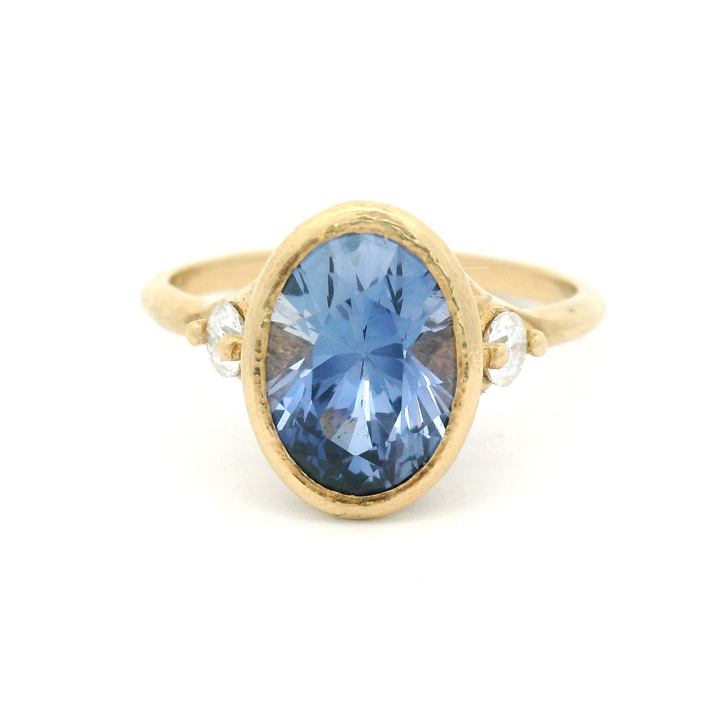 10K yellow gold organic three-stone engagement ring with a bezel-set 3ct lab-grown oval blue sapphire and two claw-set moissanite shoulder stones.