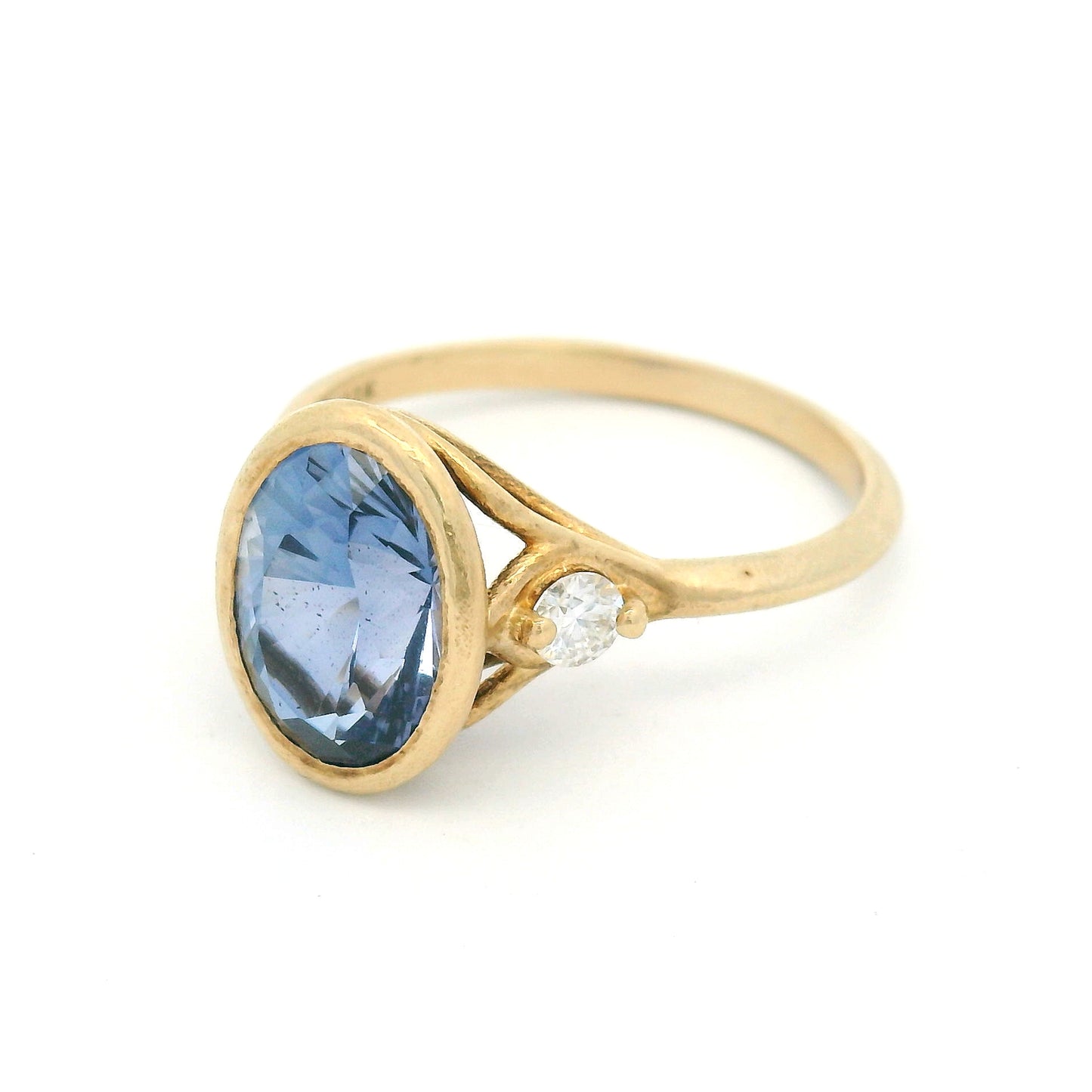 10K yellow gold organic three-stone engagement ring with a bezel-set 3ct lab-grown oval blue sapphire and two claw-set moissanite shoulder stones.