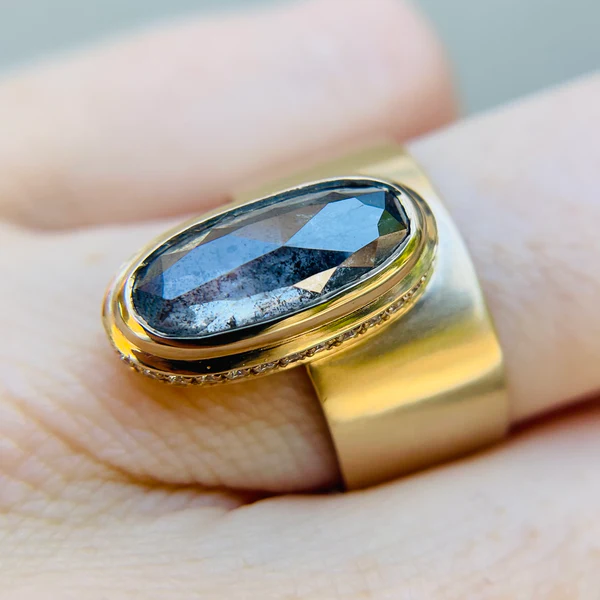 14k yellow gold ring set with a 3.18ct salt and pepper elongated oval rose cut diamond with hidden pave diamonds.  Shown on a finger.