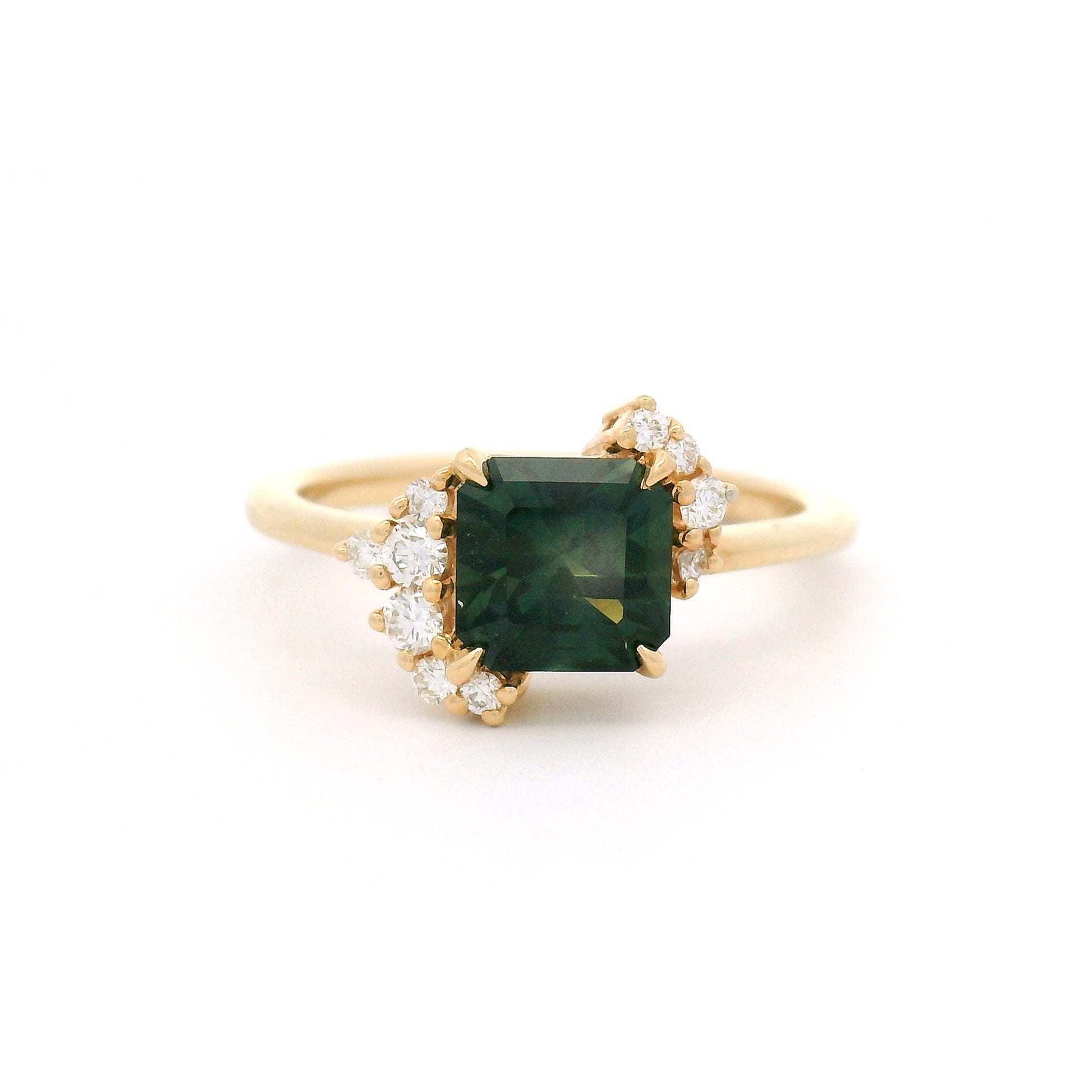 14K yellow gold asymmetrical engagement ring featuring a claw-set natural 1.41ct square radiant-cut dark green-teal sapphire with 10 claw-set natural diamond accents totalling 0.16cts on a delicate 1.7mm band.