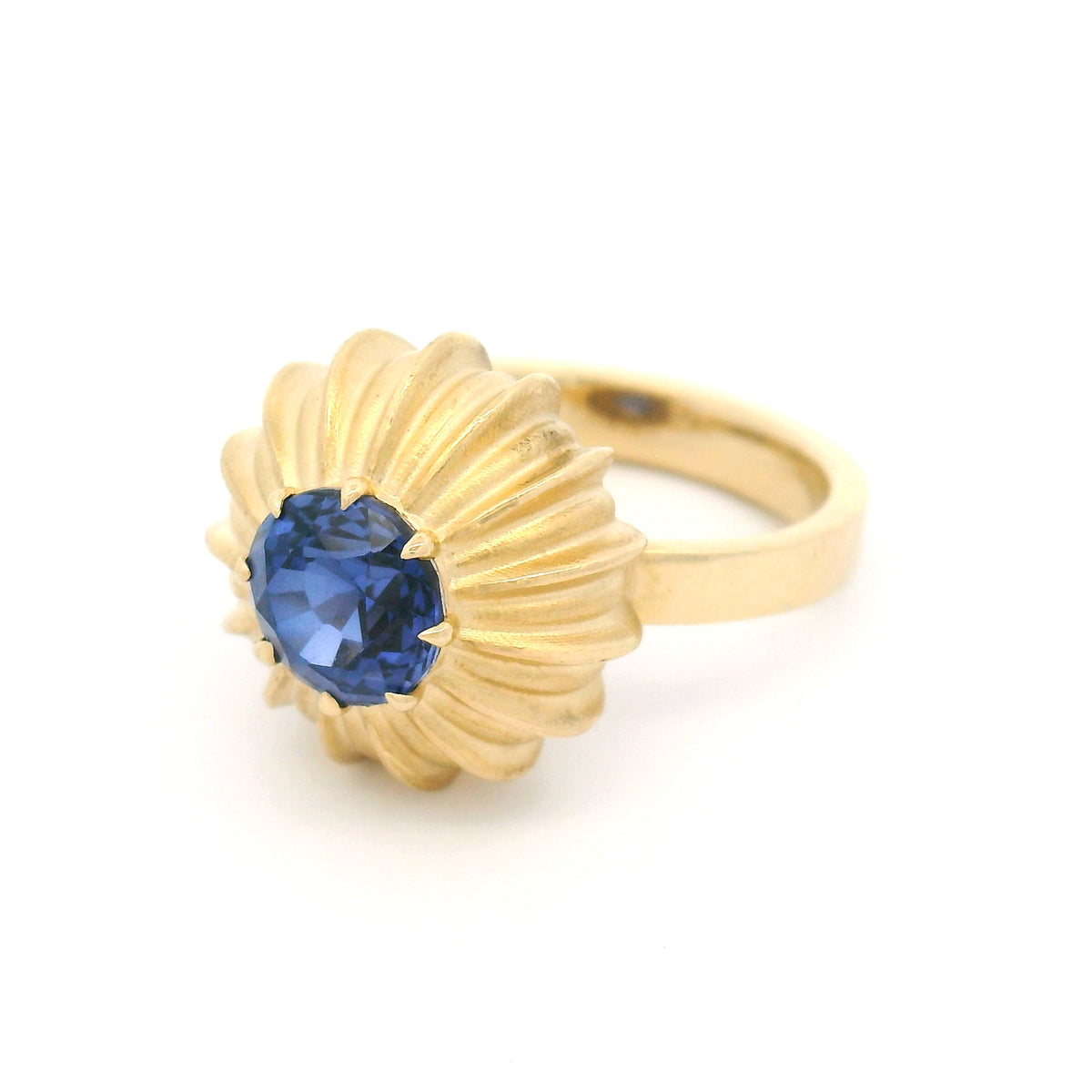 14K yellow gold claw-set solitaire engagement ring featuring a 6.6mm lab-grown round blue sapphire in a sculptural fluted sunburst setting.
