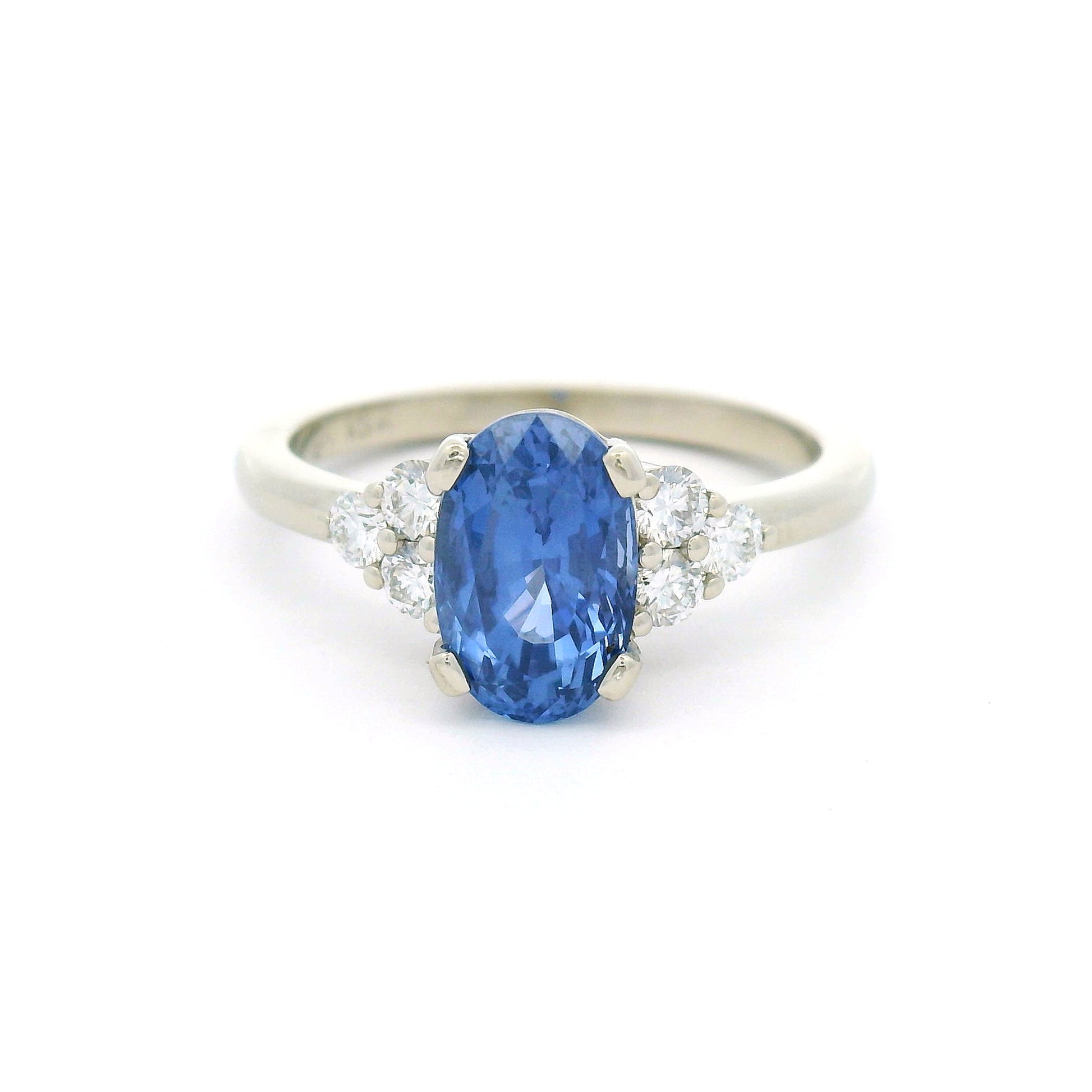 18K white gold engagement ring featuring a claw-set natural unheated 2.39ct oval blue sapphire with two trios of claw-set natural diamonds totalling 0.29cts on the shoulders.