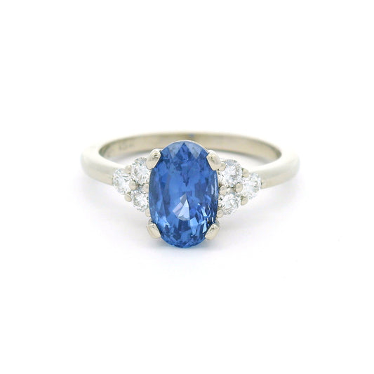 18K white gold engagement ring featuring a claw-set natural unheated 2.39ct oval blue sapphire with two trios of claw-set natural diamonds totalling 0.29cts on the shoulders.