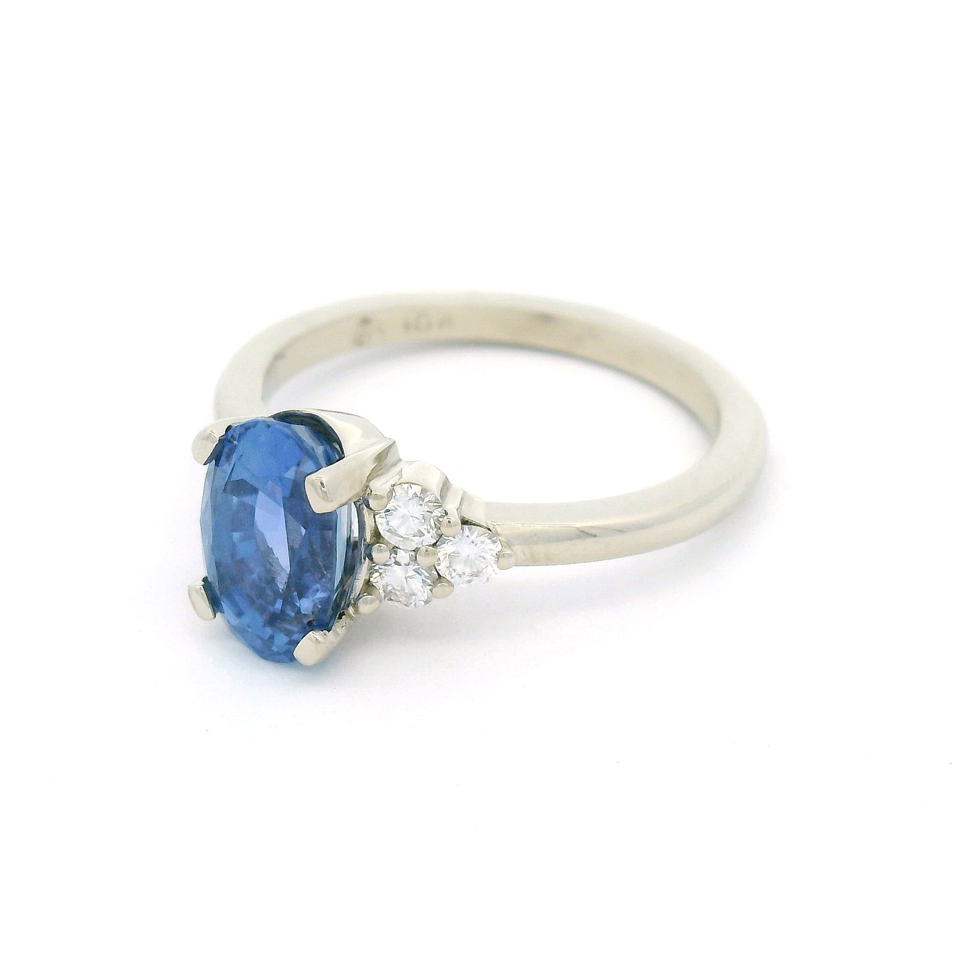 18K white gold engagement ring featuring a claw-set natural unheated 2.39ct oval blue sapphire with two trios of claw-set natural diamonds totalling 0.29cts on the shoulders.