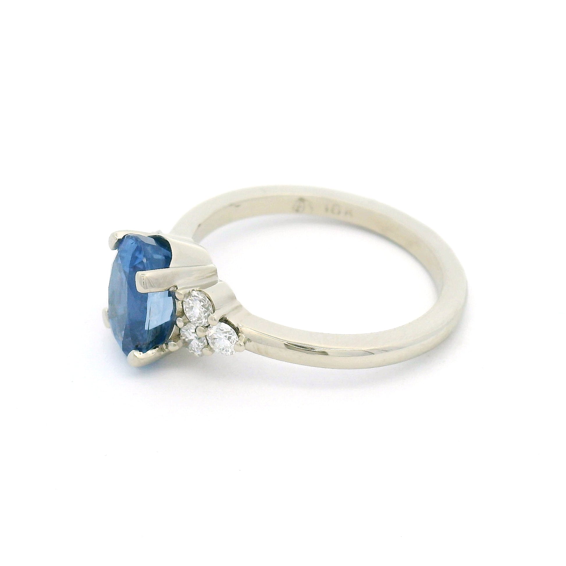 18K white gold engagement ring featuring a claw-set natural unheated 2.39ct oval blue sapphire with two trios of claw-set natural diamonds totalling 0.29cts on the shoulders.