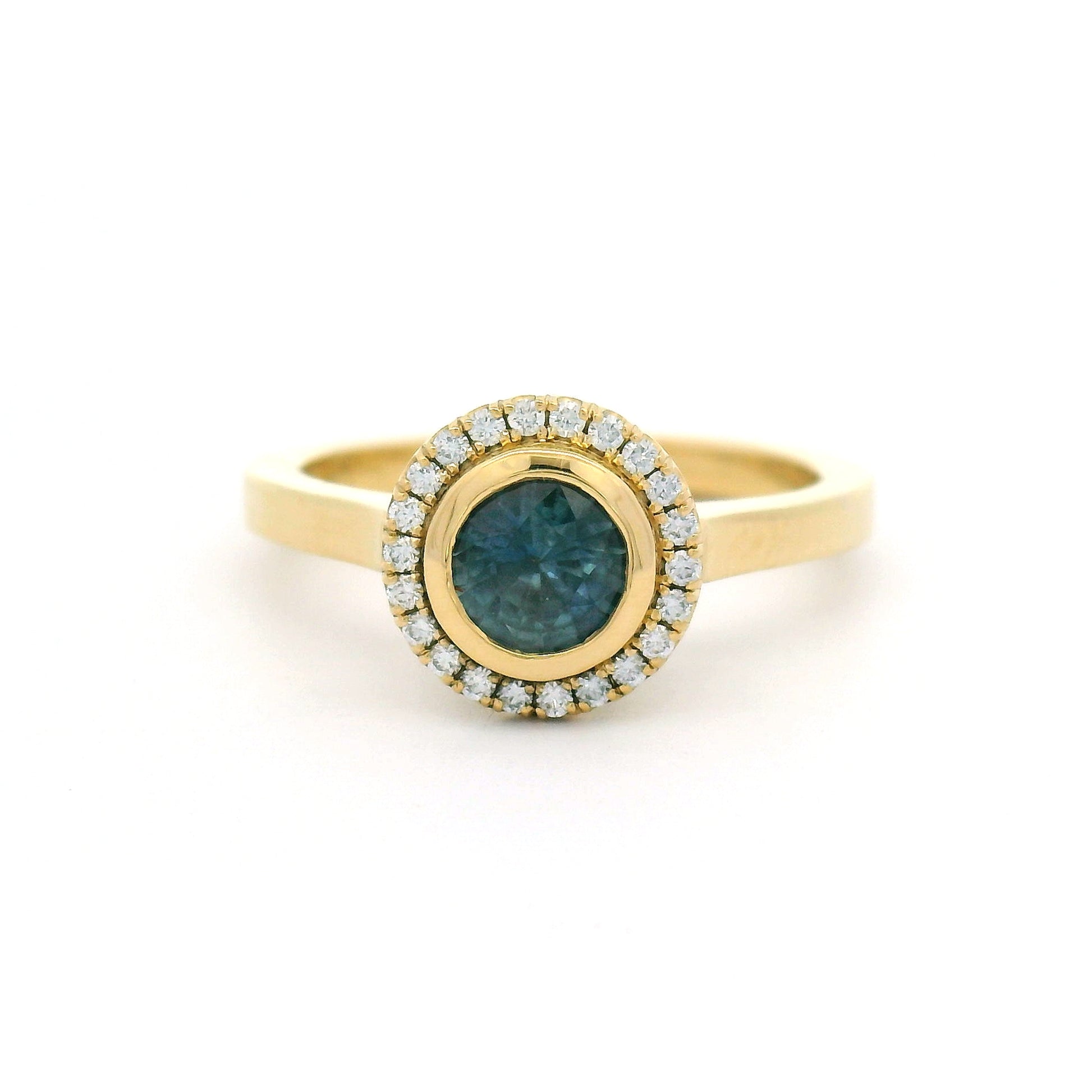 18K yellow gold engagement ring with a bezel-set natural 0.65ct round teal sapphire and bead-set halo of 0.12cts natural diamonds.