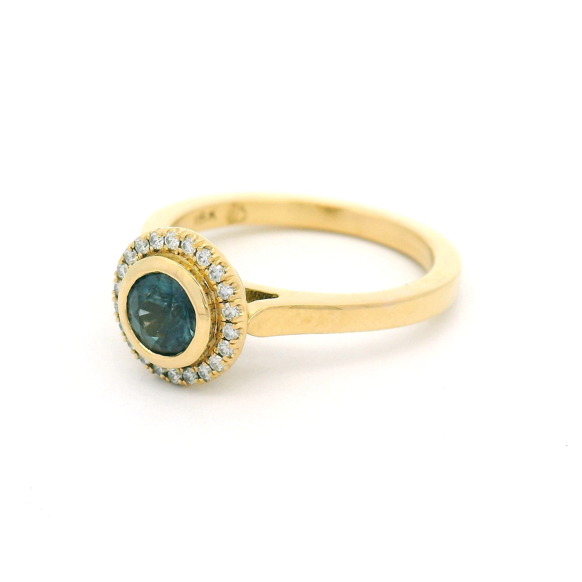 18K yellow gold engagement ring with a bezel-set natural 0.65ct round teal sapphire and bead-set halo of 0.12cts natural diamonds.