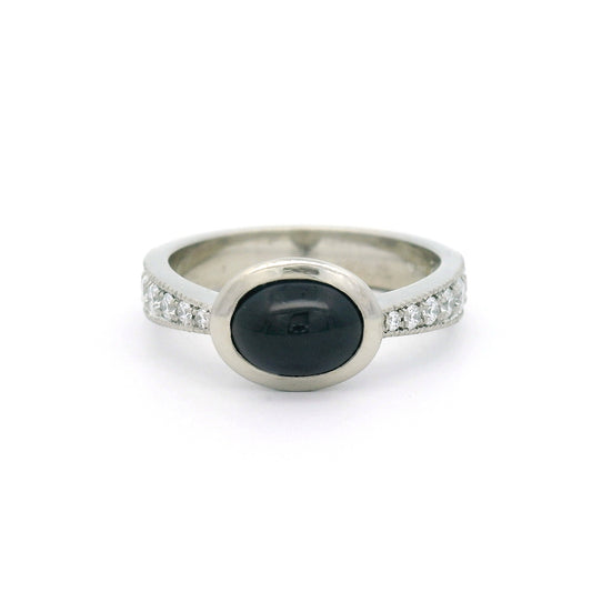 18K white gold bezel-set engagement ring with a natural 2.23ct oval cabochon blue sapphire and tapered band featuring 12 natural round brilliant-cut diamonds.