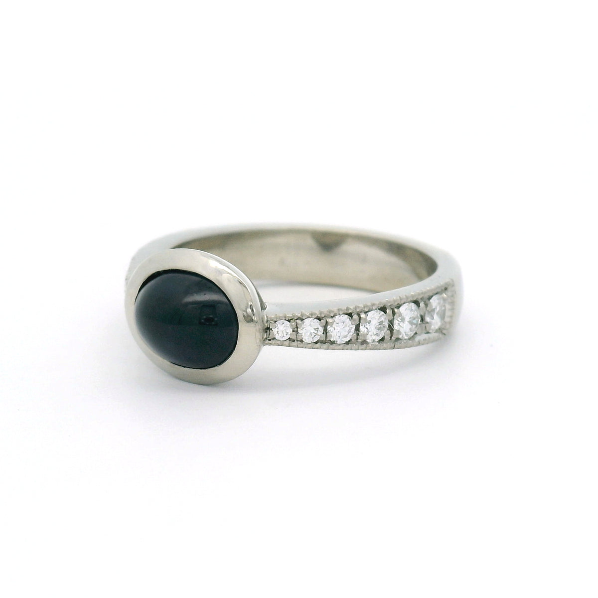 18K white gold bezel-set engagement ring with a natural 2.23ct oval cabochon blue sapphire and tapered band featuring 12 natural round brilliant-cut diamonds.