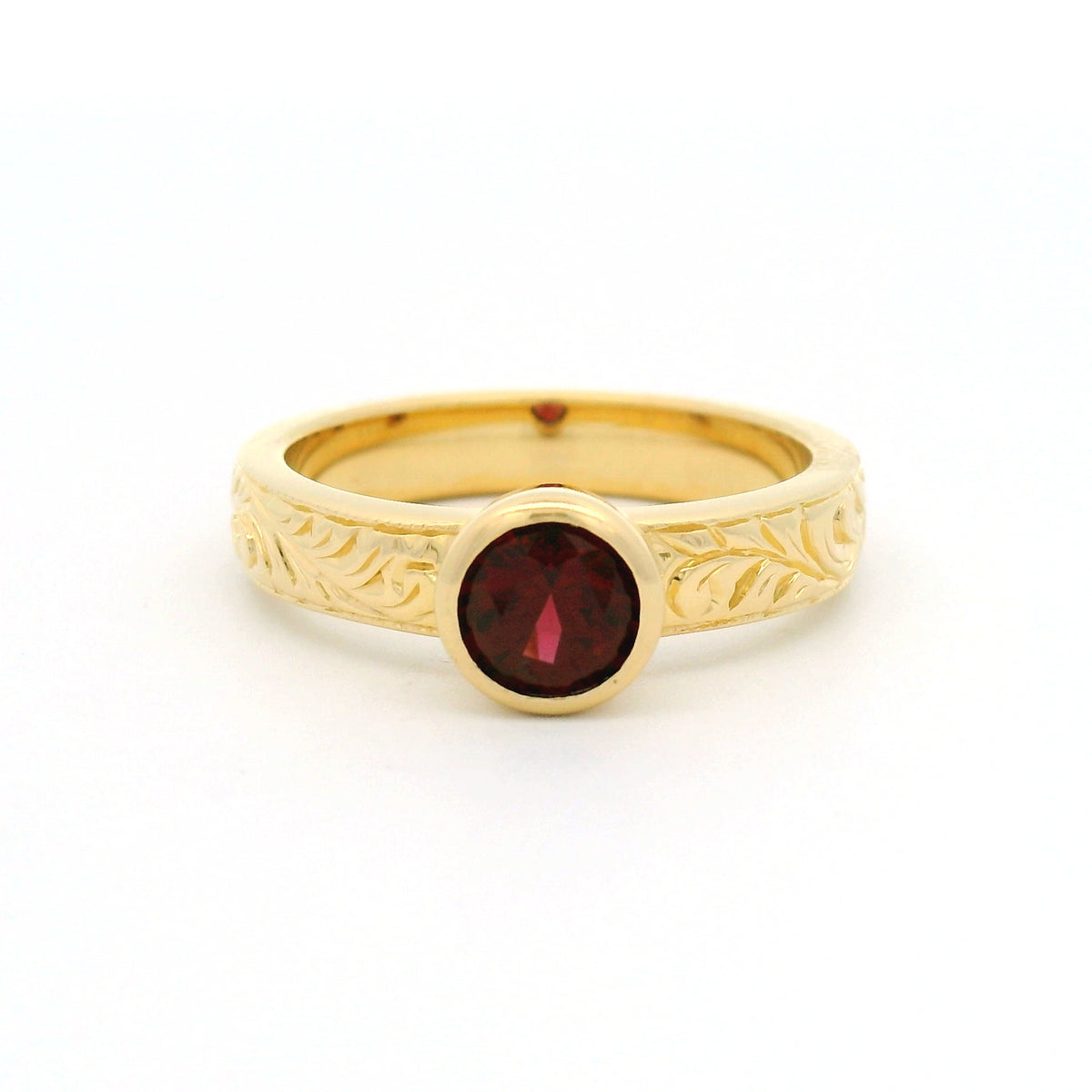 18K yellow gold bezel-set solitaire ring with a natural 0.68ct round red spinel and nature-inspired hand engraving on the 3.8mm band.