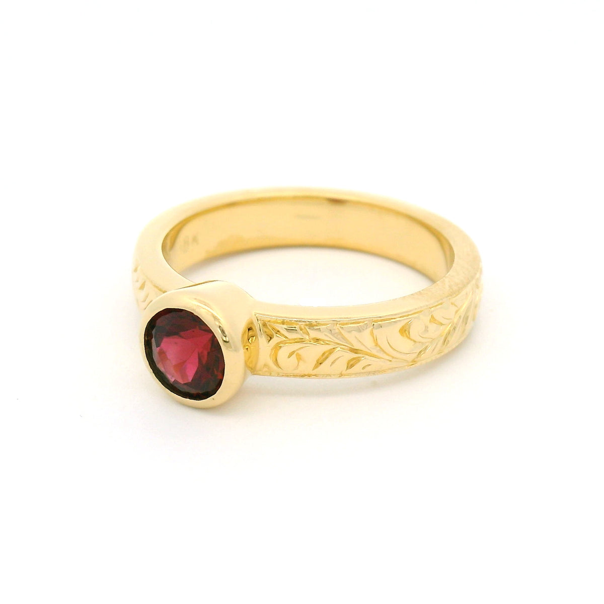 18K yellow gold bezel-set solitaire ring with a natural 0.68ct round red spinel and nature-inspired hand engraving on the 3.8mm band.