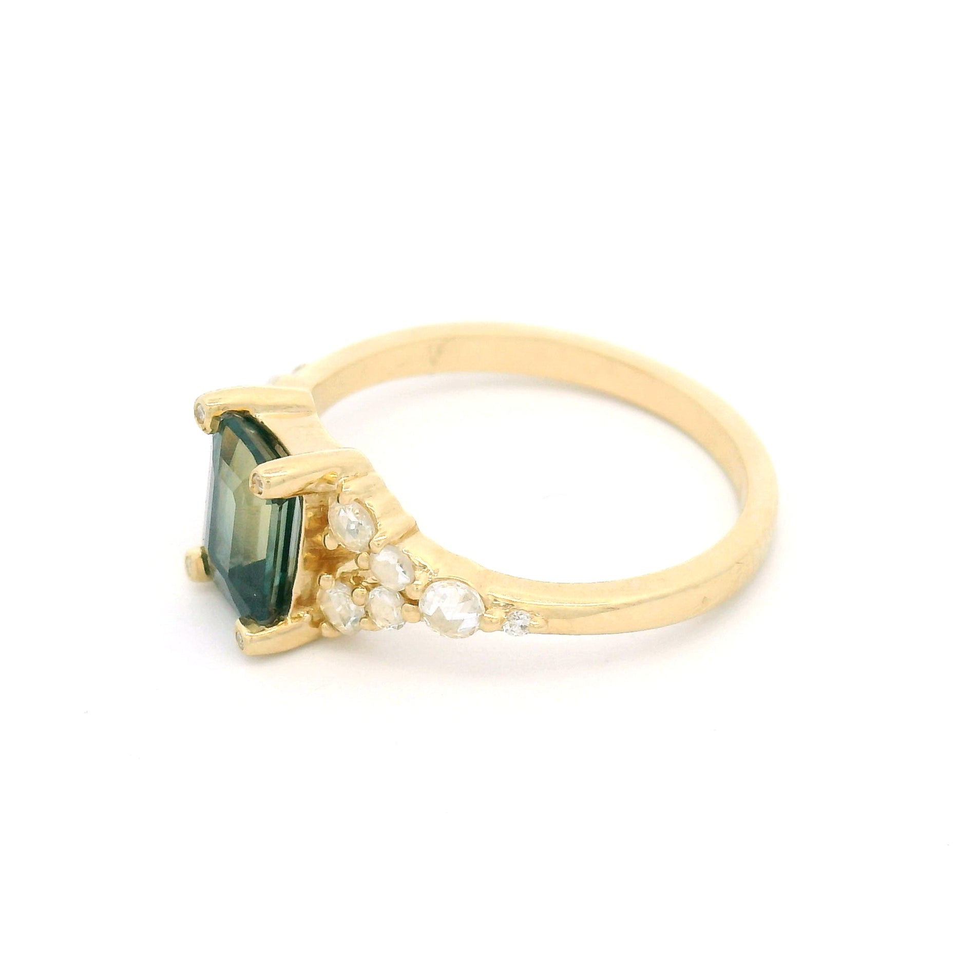 14K yellow gold split shank engagement ring featuring a 1.25ct emerald-cut bluish-green bi-colour sapphire with rose-cut and round brilliant-cut diamond accents.