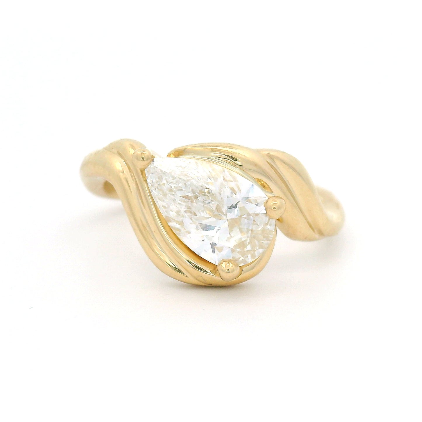 14K yellow gold low-profile solitaire engagement ring with a claw-set 1.25ct pear-shaped lab-grown diamond and sculptural ribbon-like setting.