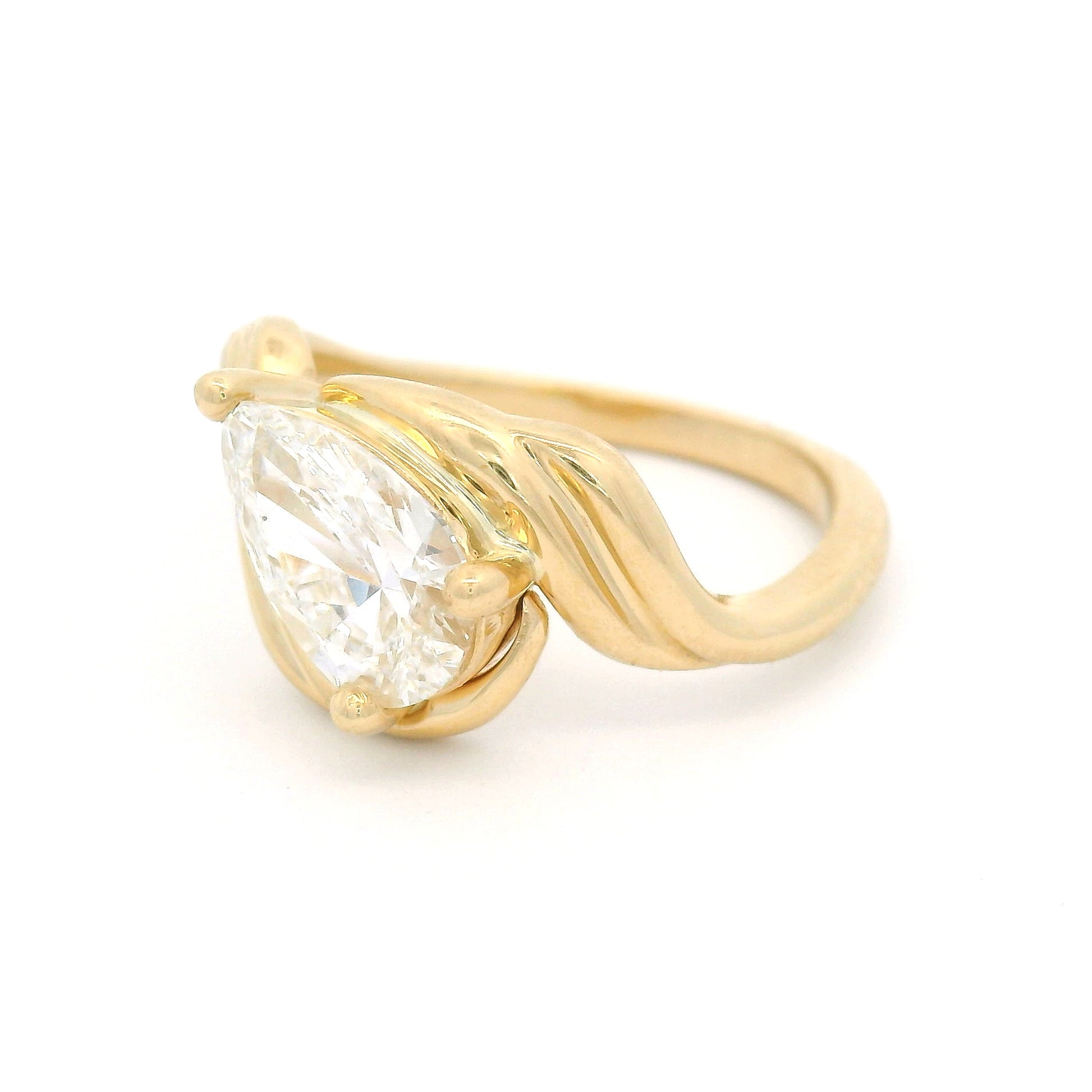 14K yellow gold low-profile solitaire engagement ring with a claw-set 1.25ct pear-shaped lab-grown diamond and sculptural ribbon-like setting.