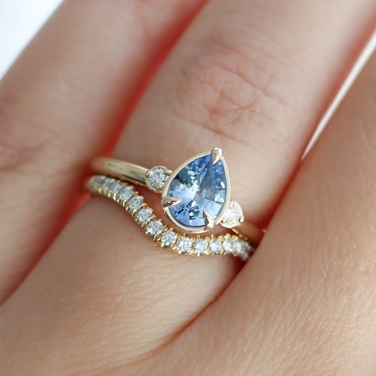 14k Yellow Three Stone Engagement Ring with 0.92ct Blue Sapphire and Accent Diamonds.  Shown on a hand with a contoured wedding band